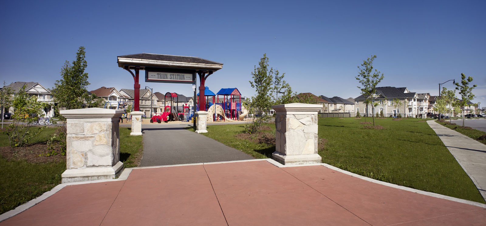 A community park in Castlegate with a Train Station pavilion, colorful children's playground, stone pillar entrance and landscaped lawns
